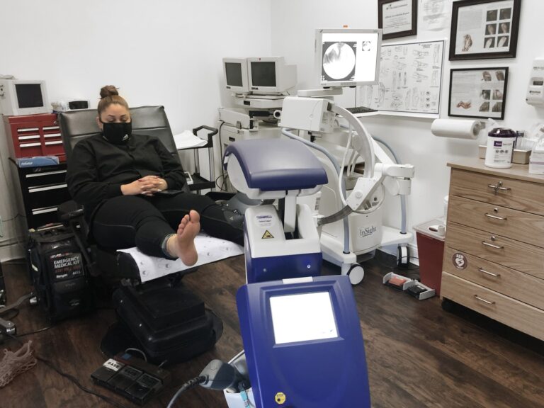 Patient reclined in a treatment chair with her bare foot positioned for laser therapy in the clinic