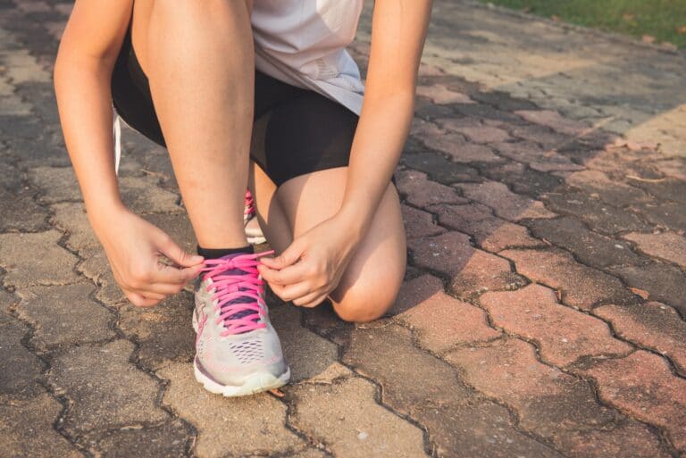 Runner kneeling on a paved path to tie the pink laces of a trainer