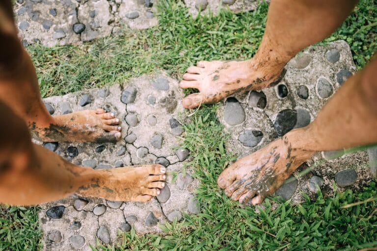 Four bare feet caked in mud standing on a cobbled garden path