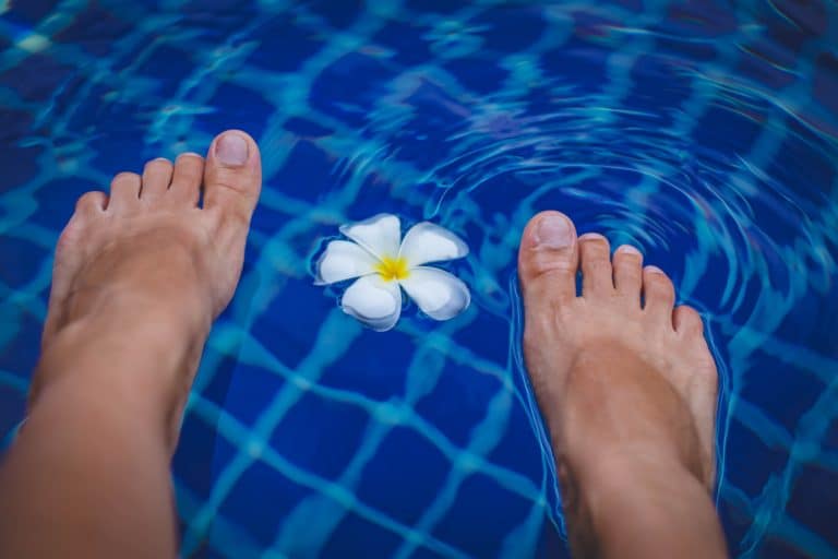 Two bare feet dipped into a swimming pool beside a floating frangipani flower