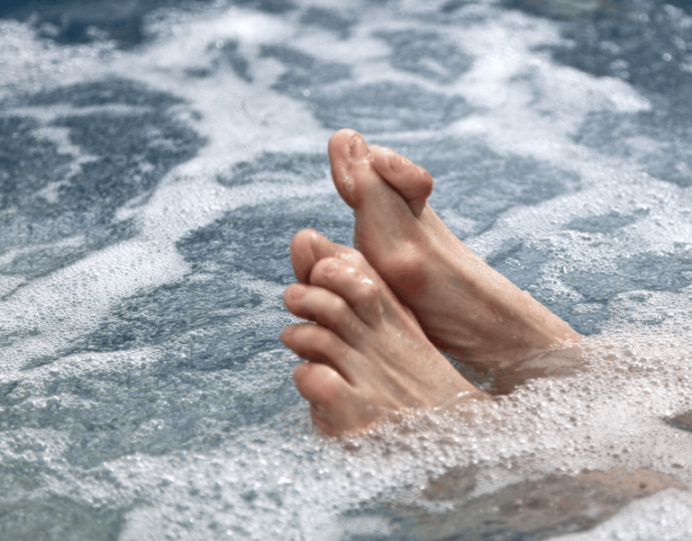 Two bare feet with curled toes resting in the bubbling water of a hot tub