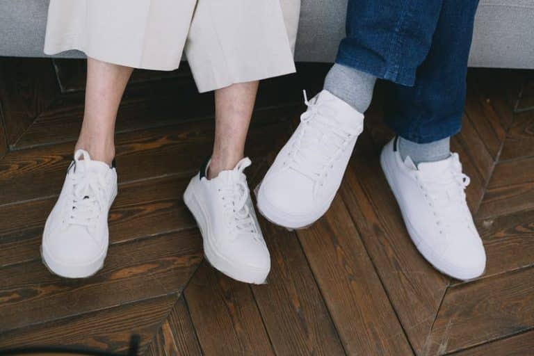 Two people seated side by side wearing white trainers on a wooden floor