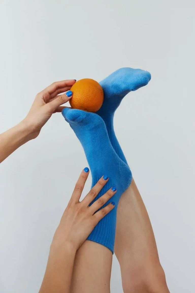 Legs raised in blue compression socks, one hand balancing an orange on a foot
