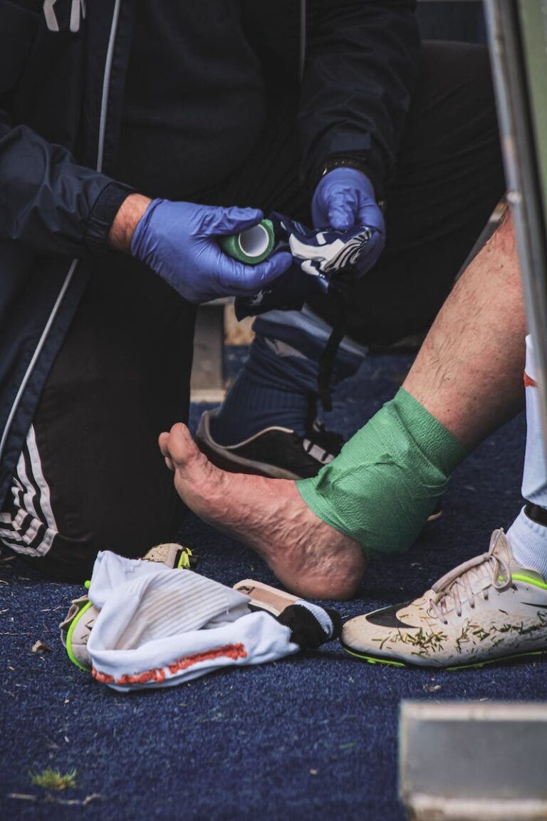 Pitch-side medic in blue gloves strapping a player's ankle with green tape