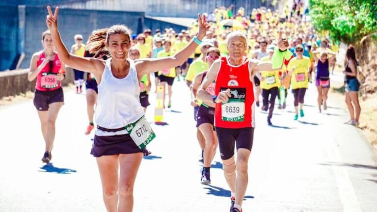 Runners on a road marathon course, a woman in front raising both arms in celebration