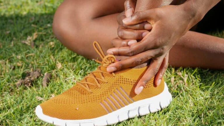Person sitting on grass in a yellow trainer holding their ankle with both hands