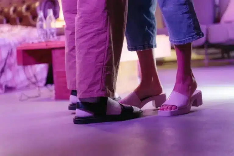 Two people standing in sandals and open-toe shoes under pink lighting