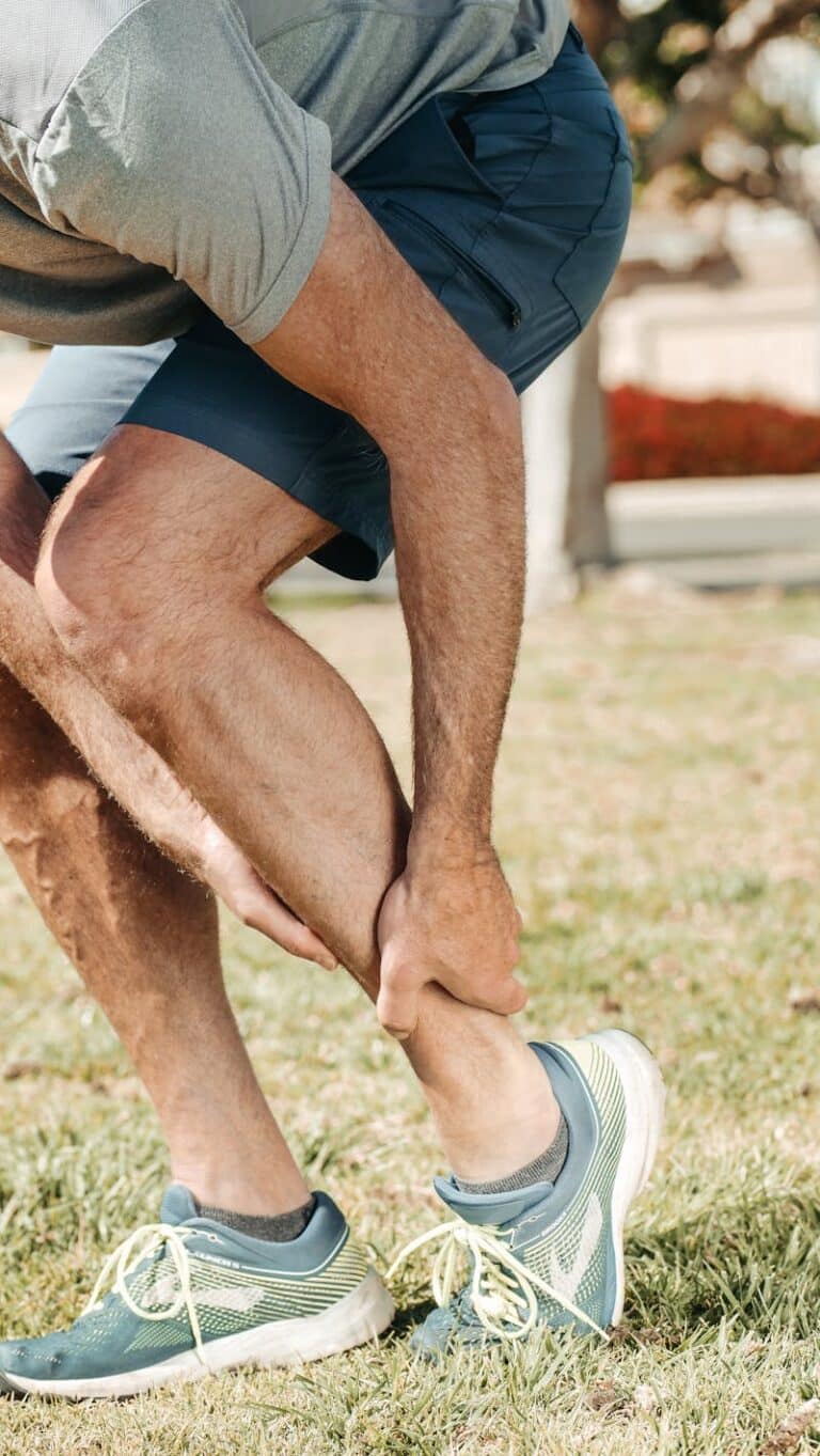 Man in sportswear bending outdoors to hold his lower leg above the ankle