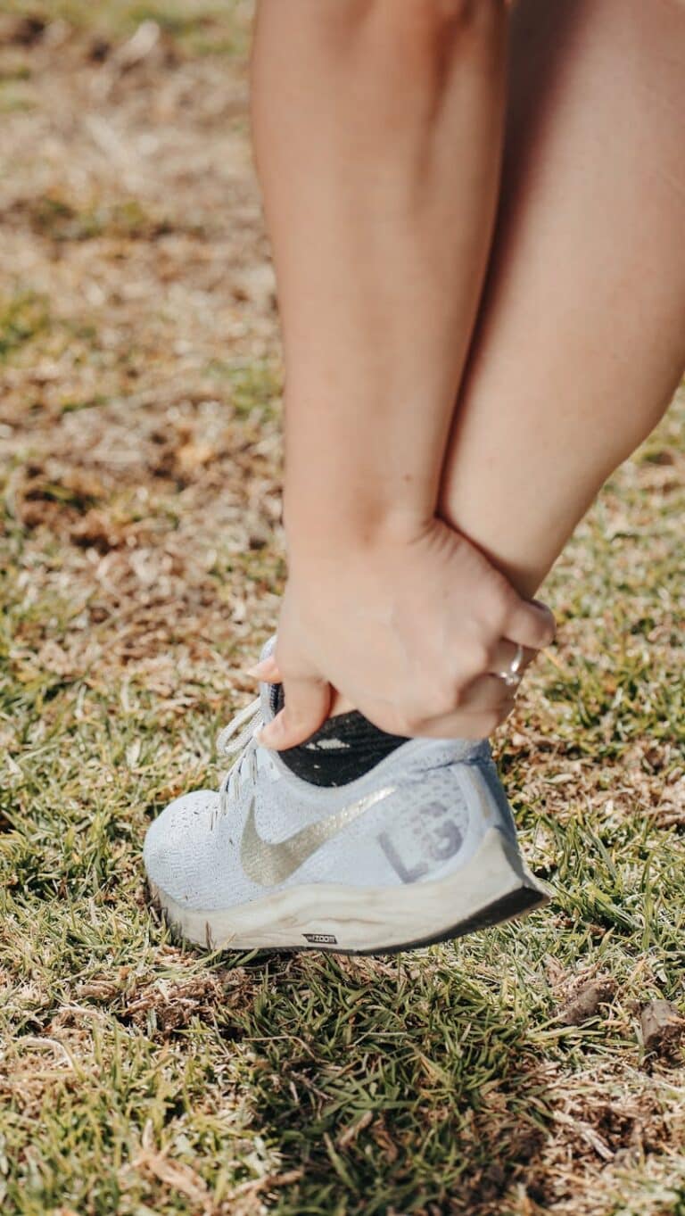 Runner outdoors on grass gripping a painful ankle above their trainer