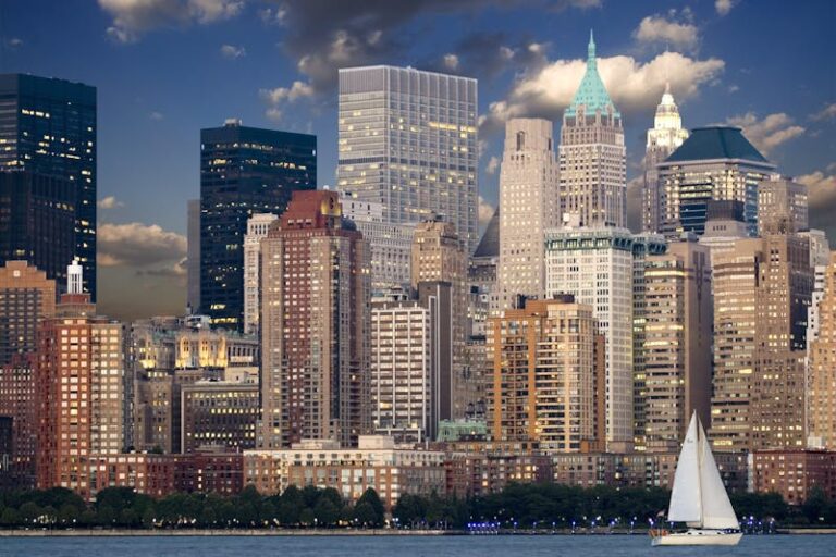 The Lower Manhattan skyline at dusk with a sailboat on the water