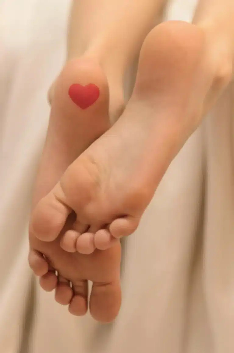 Two bare soles resting together with a small red heart sticker on one heel