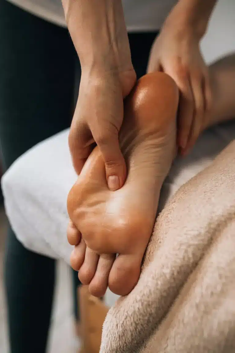Therapist's hands massaging the sole of an oiled foot resting on a towel
